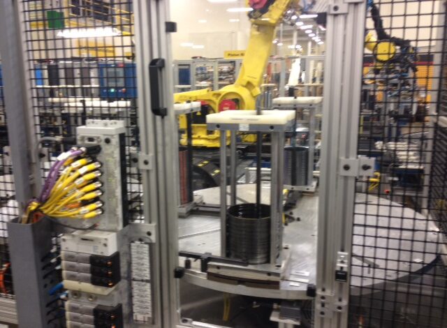 Industrial robot arm operating in a machine tool factory, surrounded by wiring and equipment.