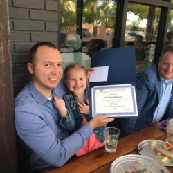 Man and child celebrate with certificate at outdoor restaurant table.
