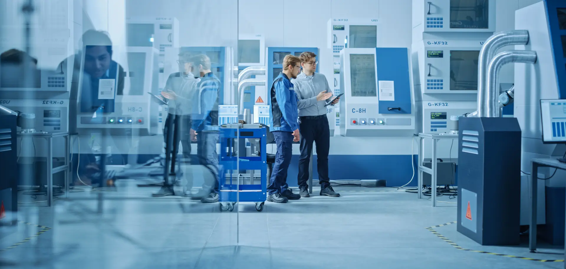 In Factory Workshop: Workers Use High-Tech Industrial CNC Machinery. Two Engineering Professional Talking and Using Digital Tablet.